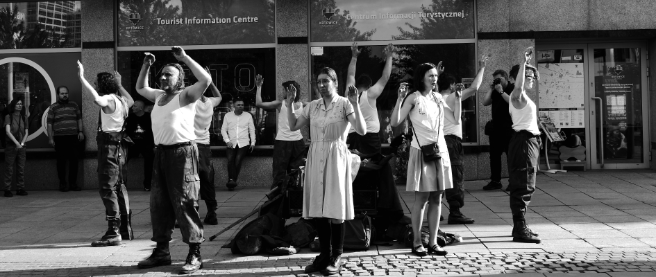 Na zdjęciu grupa ludzi stojąca w okręgu, twarzami zwrócona do widza, wszyscy mają uniesione w góre ręce