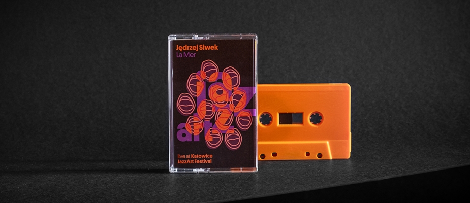 zdjęcie kasety magnetofonowej - pomarańczowa kaseta, okładka w identyfikacji jazzartu (krzyczące usta z wpisanym logo festiwalu). Podpis: Jędrzej Siwek La Mer live at Ktowice JazzArt Festival
