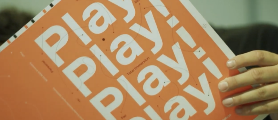 Pomarańczowa okładka aplikacji w wersji książkowej z napisem Play! Play! Play! Play!